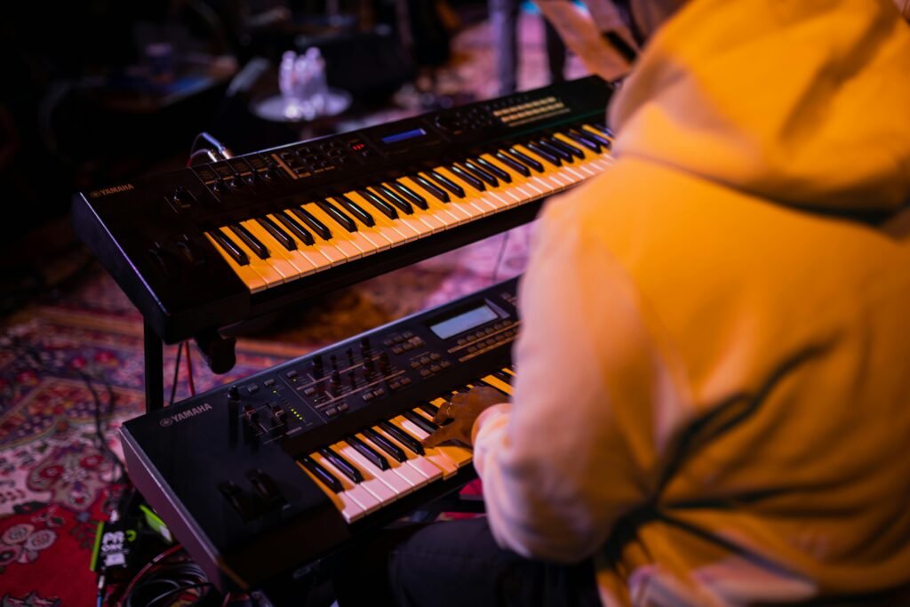 A musician playing two electronic keyboards, captured from behind during a session in a studio setting.